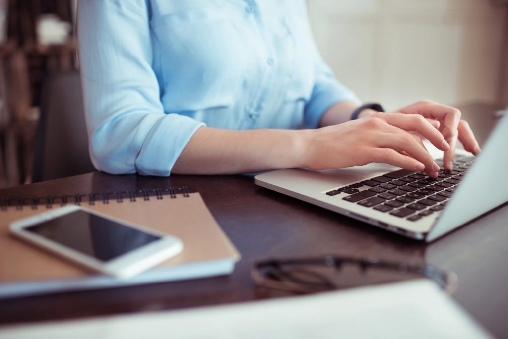 Frau in heller Bluse sitzt im Büro einer Steuerberatung und arbeitet am Laptop